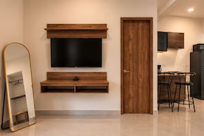A modern living room with a flat-screen TV mounted on a wooden wall unit, a door leading to a kitchen area, and a dining table with bar stools. - La Palma Experience (Panama City)
