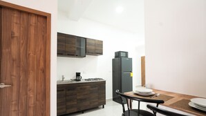 A compact kitchen with dark wooden cabinets, a black refrigerator, a coffee maker, and a dining table with chairs. - La Palma Experience (Panama City)