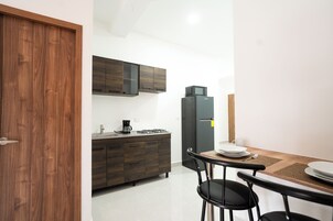Una cocina compacta con armarios de madera oscura, un refrigerador negro, una cafetera y una mesa de comedor con sillas.