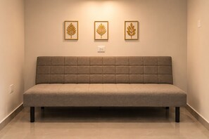 A neutral-toned sofa with a padded backrest and armrests, positioned against a wall with three framed leaf designs. - La Palma Experience (Panama City)