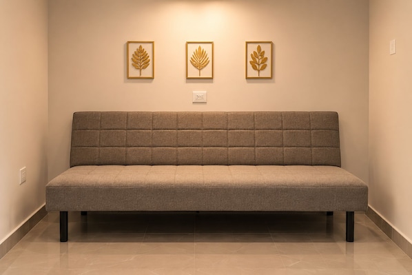 A neutral-toned sofa with a padded backrest and armrests, positioned against a wall with three framed leaf designs. - La Palma Experience (Panama City)
