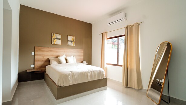 Ein modernes Schlafzimmer mit einem großen Bett, einem Nachttisch, einer Wand-Klimaanlage und einem Fenster mit Vorhängen.