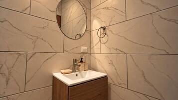 Une salle de bain avec un mur recouvert de carreaux de marbre, un meuble en bois, un lavabo blanc, un miroir et un porte-serviettes.