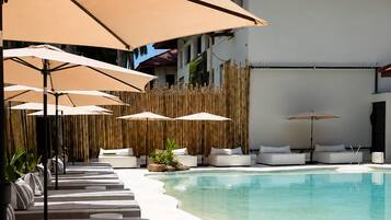 A poolside area with lounge chairs and umbrellas, a clear pool, and a building with a red roof.