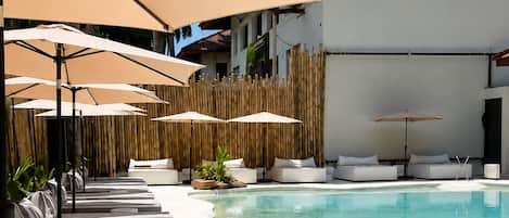 A poolside area with lounge chairs and umbrellas, a clear pool, and a building with a red roof.