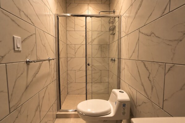 A bathroom with a shower stall, toilet, and marble walls. - La Palma Experience (Panama City)
