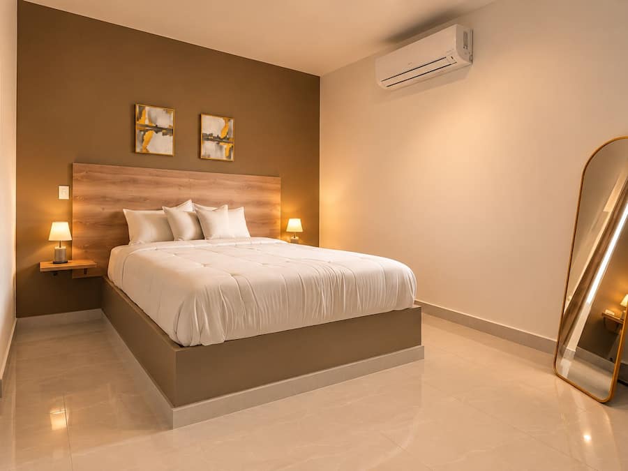 Quarto moderno com uma cama grande, abajures, ar condicionado e espelho de corpo inteiro.