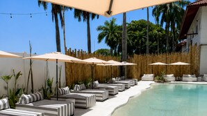 A poolside area with striped lounge chairs and umbrellas, surrounded by a bamboo fence and palm trees. - La Palma Experience (Panama City)