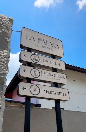 Ein Wegweiser mit mehreren Pfeilen, die zu verschiedenen Einrichtungen wie Schwimmbadclub, Restaurant und Apartments zeigen.