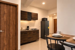 Cozinha compacta com armários de madeira, geladeira preta, micro-ondas e cafeteira.