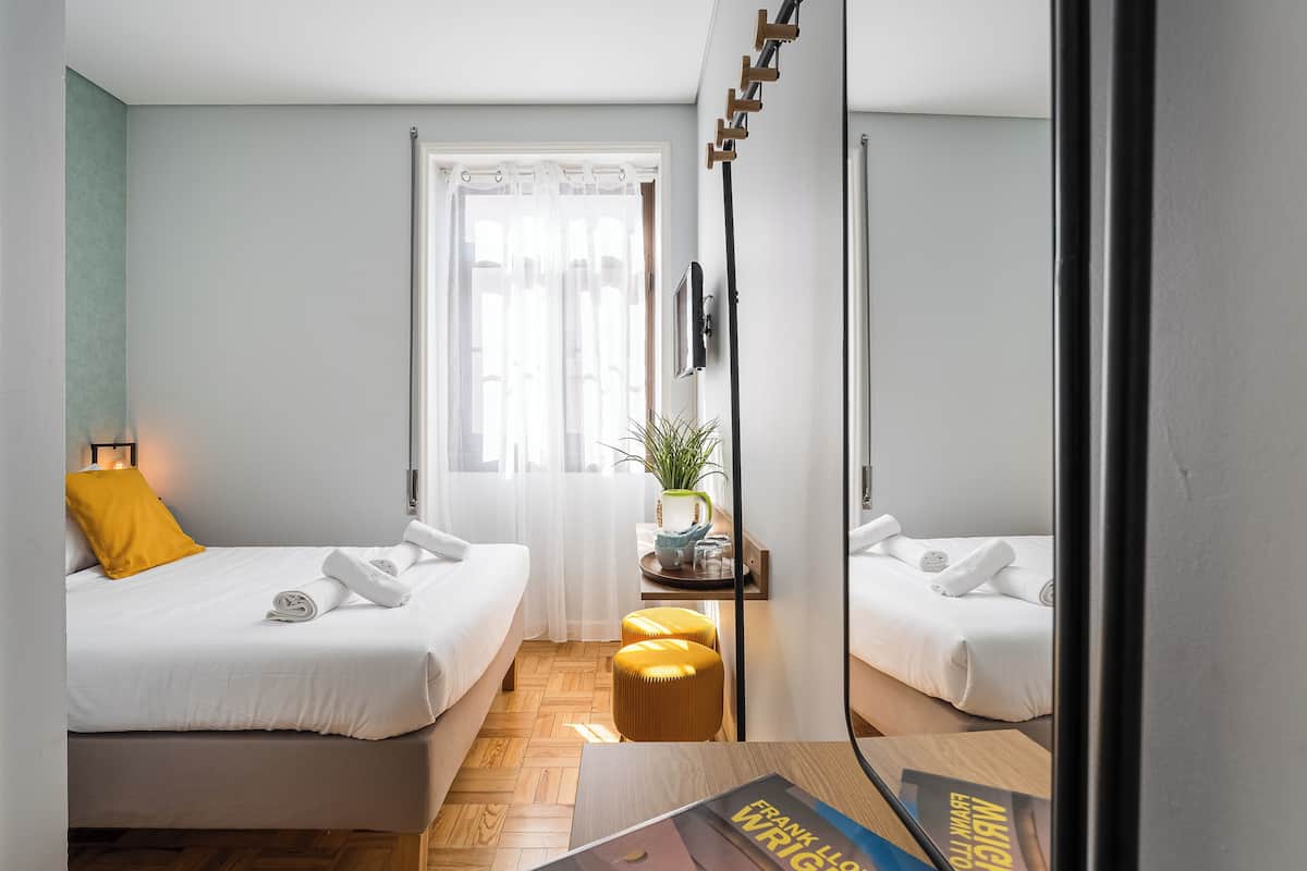 Una moderna camera d'albergo con due letti, un tavolino con una pianta, uno specchio e una finestra con tende.