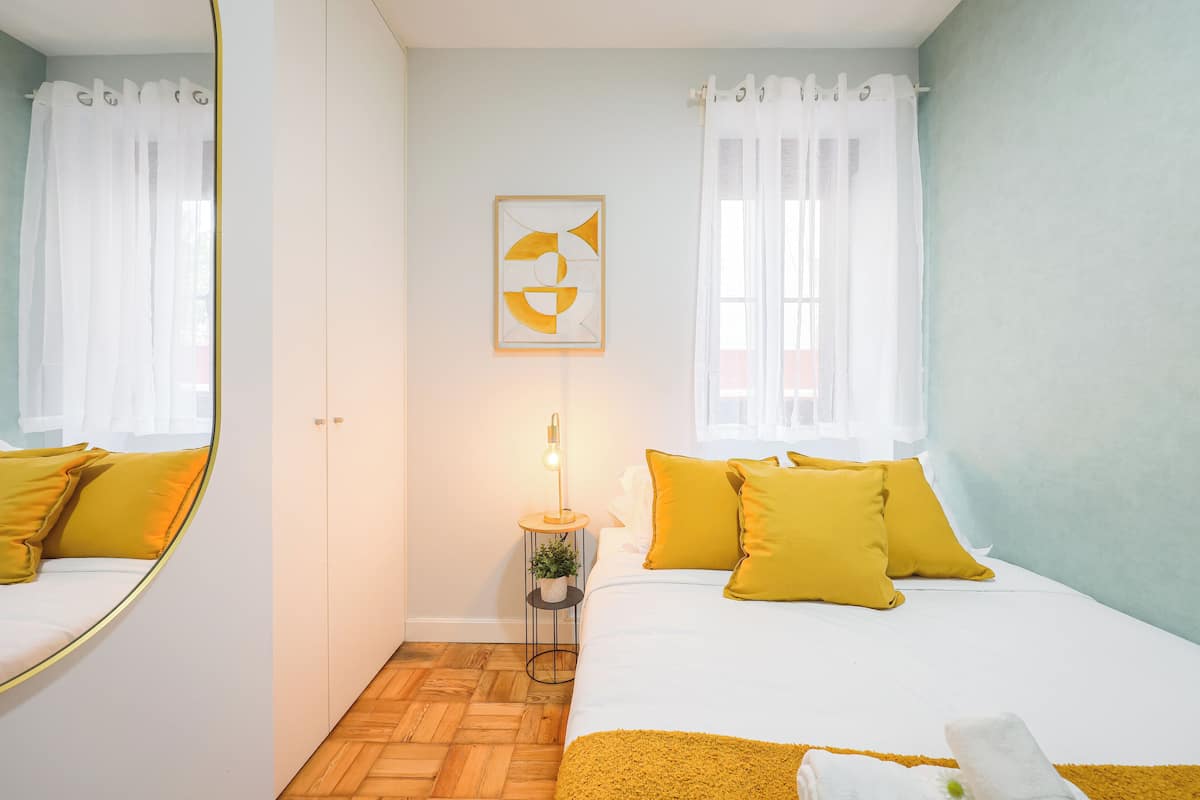 Una camera da letto con un letto, un comodino con una lampada, un’opera d’arte appesa al muro e una finestra con tende.