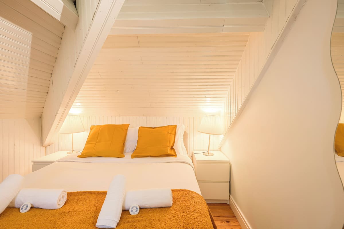 Una camera da letto con un letto, due comodini, una lampada e un asciugamano arrotolato sul letto.