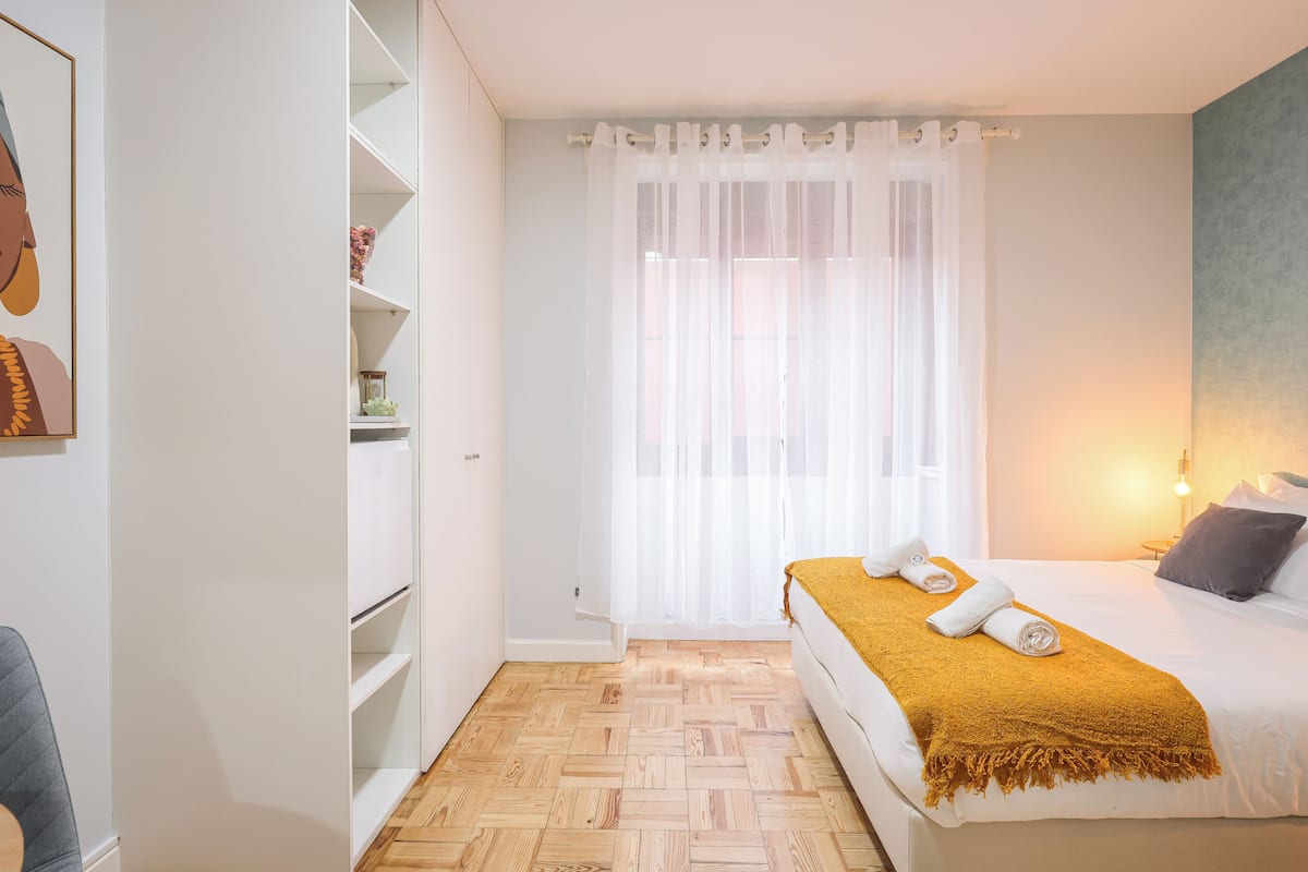 Una camera da letto con un letto, una finestra con tende leggere, un comodino con una lampada e un armadio.