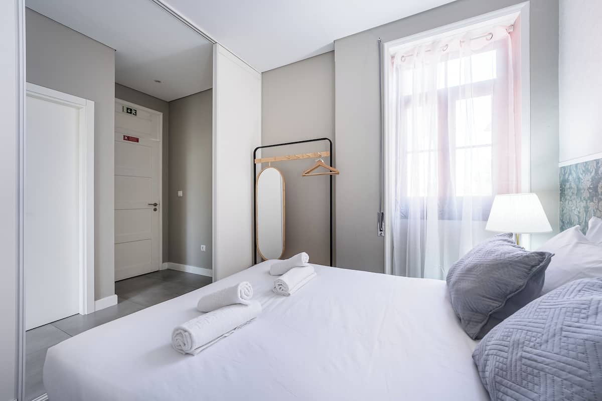 Una camera d'albergo con un letto, uno specchio, un appendiabiti e una finestra con tende.