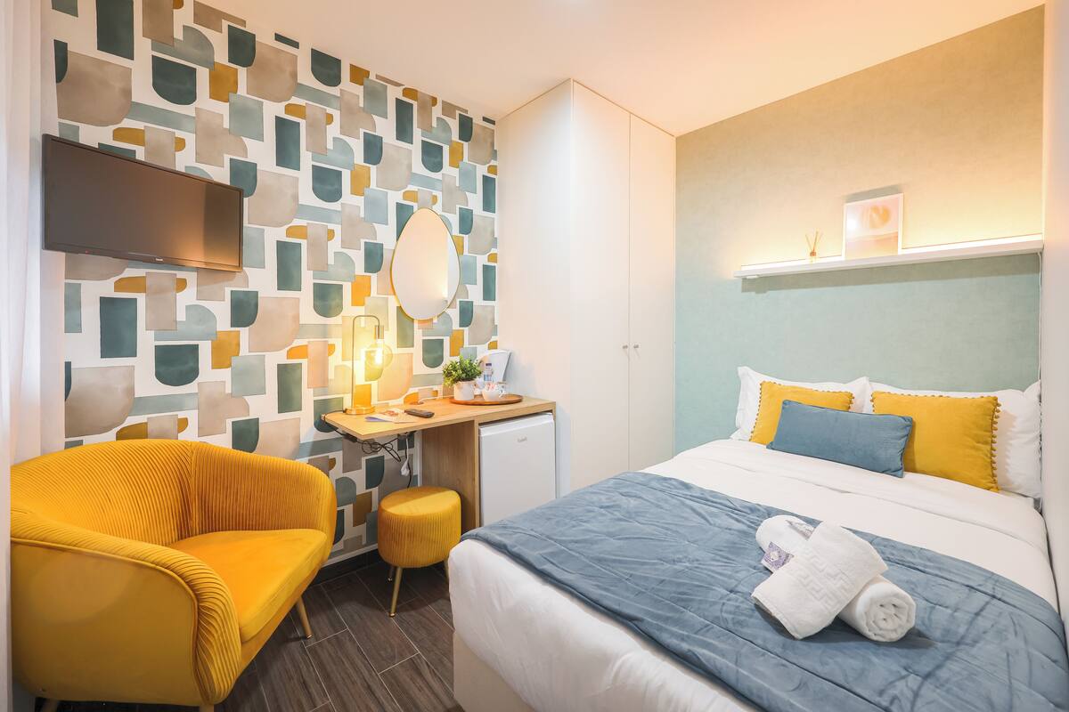 Una camera d'albergo con un letto, una scrivania, una sedia, una televisione e una parete con motivo geometrico.