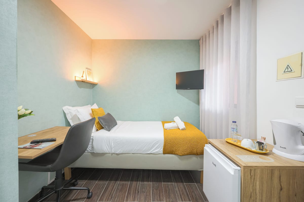 Una camera d'albergo con un letto, una scrivania, una sedia, un televisore, un bollitore e un tavolino con vassoio.