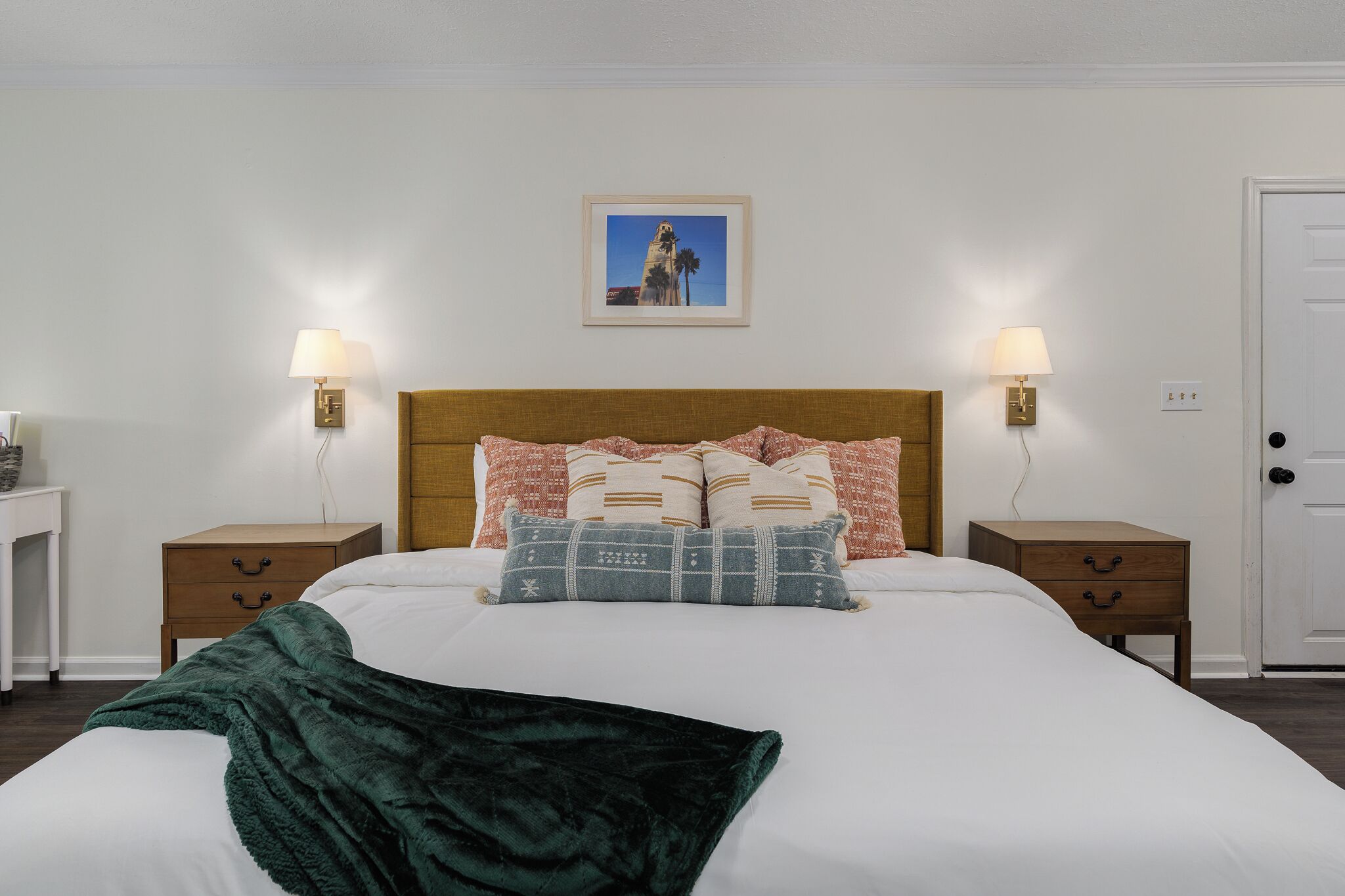 A neatly made bed with a green throw blanket, two bedside tables with lamps, and a framed picture on the wall.