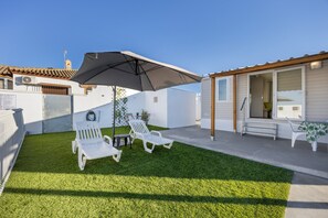 A patio with two white lounge chairs, a table, and a large umbrella.