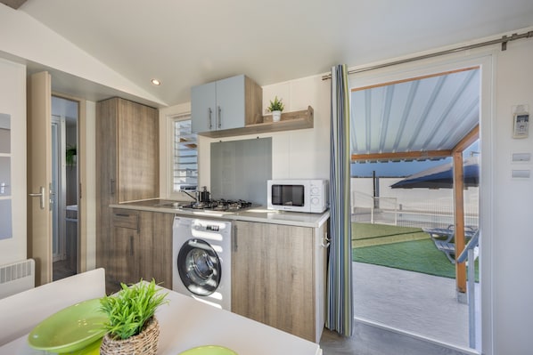 A compact kitchen with a washing machine, microwave, and a small dining area with a green table.