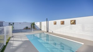 Une piscine entourée d’une clôture blanche, un ciel dégagé et un mur orné de trois carreaux décoratifs.