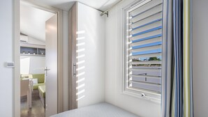 Une chambre à coucher avec un lit, une fenêtre avec des stores, une porte donnant sur une salle de bain et une vue sur l’extérieur.