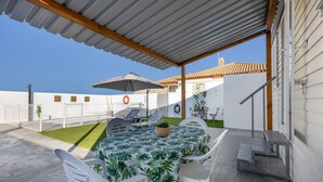 Une terrasse extérieure avec une table et des chaises, un espace abrité et une vue sur un bâtiment doté d’un toit en tuiles.