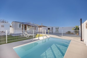 A swimming pool with a white fence, a house, and a clear blue sky.