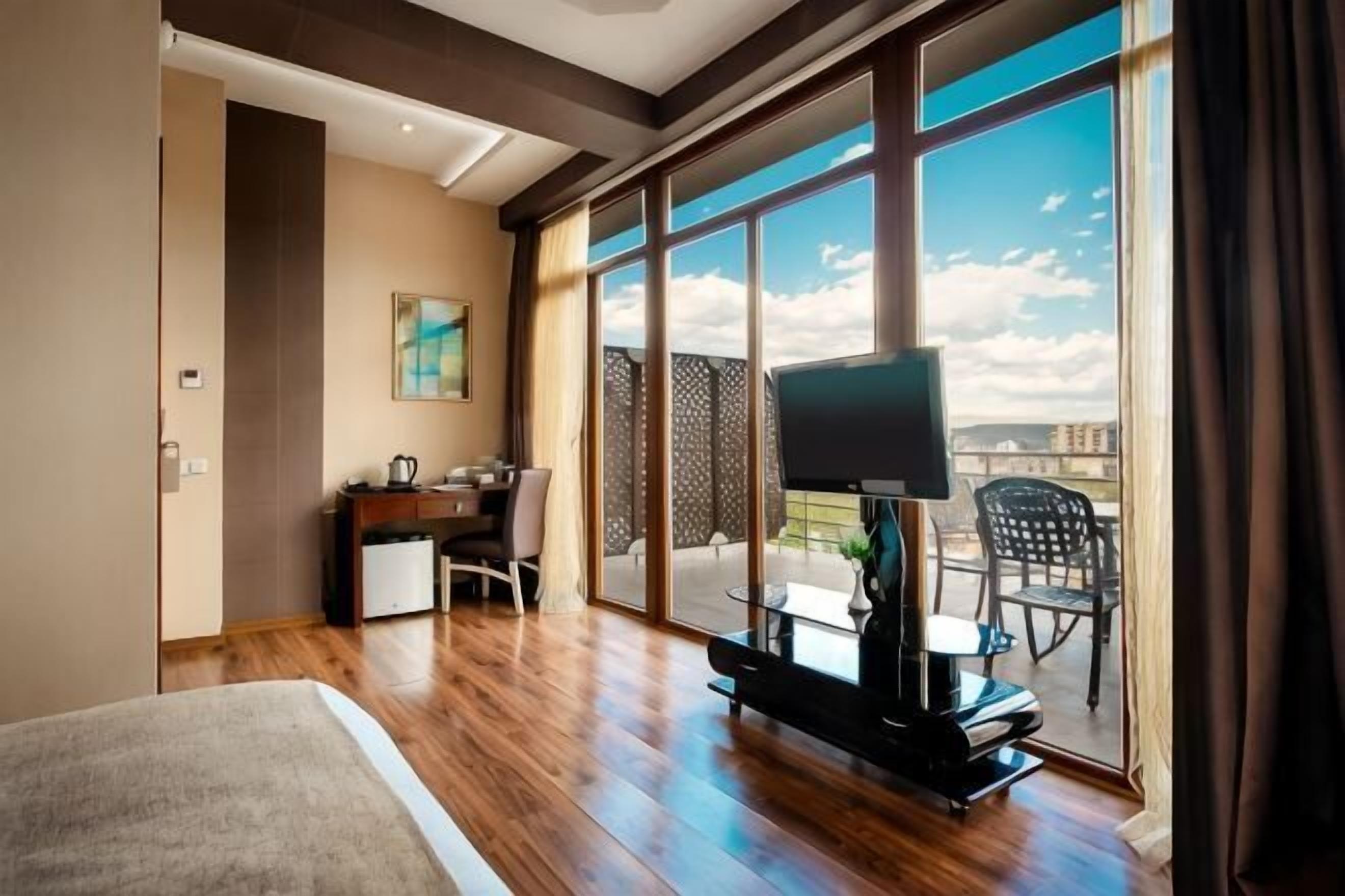 Une chambre avec un grand lit, un bureau avec une chaise, une télévision et un balcon avec des chaises.