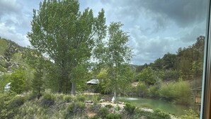 Une vue à travers une fenêtre sur un paysage naturel, avec des arbres, une rivière et un terrain vallonné.