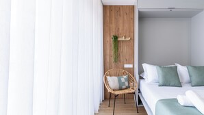 Une chambre d’hôtel moderne avec un mur d’accent en bois, un fauteuil en osier agrémenté d’un coussin, un lit soigneusement fait avec une literie verte et une plante suspendue.