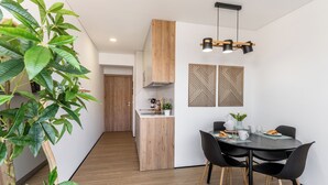 Une cuisine moderne avec des meubles en bois, une table à manger avec des chaises noires et un luminaire suspendu.