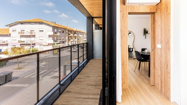 Un balcon doté d’un plancher en bois et d’une rambarde en métal, offrant une vue sur une rue et des immeubles.