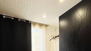 Een kamer met een zwart gordijn, een witte deur, een kledingrek met kleding en een zwarte muur met een ontwerp van een boom.