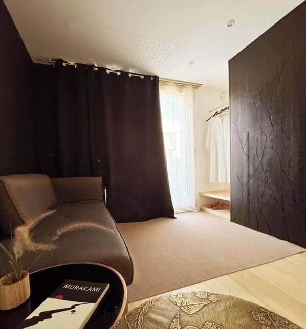 Ein modernes Zimmer mit einer Couch, einem kleinen Tisch mit einer Zeitschrift, einer Wand mit einem baumartigen Design und einem Fenster mit Vorhängen.