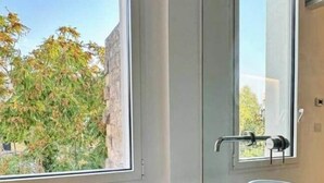 Een badkamer met twee witte wasbakken, een raam met uitzicht op bomen, en een deur met een handdoekhouder.