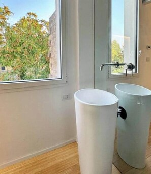 Un baño con ventana, dos lavamanos blancos y una manija de puerta a la vista.