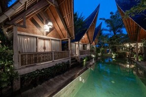Zona junto a la piscina con estructuras de madera, una piscina cristalina y vegetación circundante.