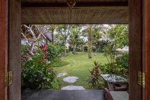 A view from a covered area to a well-maintained garden with a lawn and various plants. - Premadhan Sanctuary (Bali)