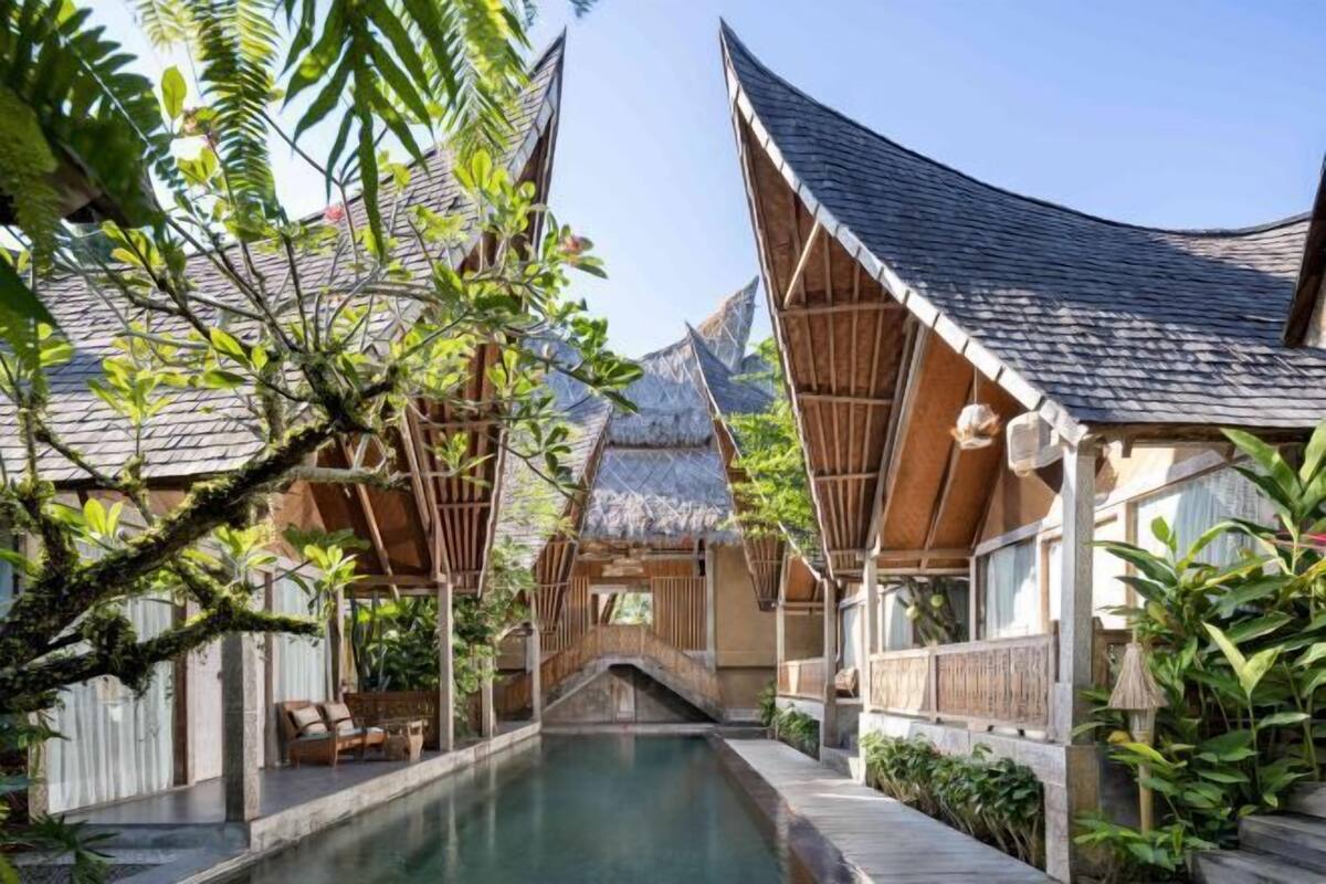 A traditional-style building with a thatched roof, a wooden deck, and a small bridge over a pool.