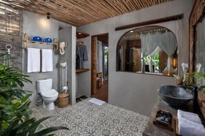 A bathroom with a patterned floor, a toilet, a sink with a large basin, and a mirror with a decorative frame. - Premadhan Sanctuary (Bali)