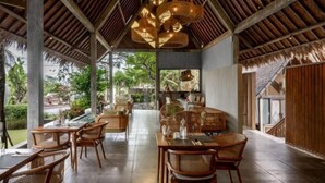 Un espace repas à aire ouverte, doté de meubles en bois et d’une structure de toit en chaume.