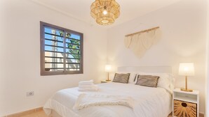 Une chambre avec un grand lit, deux tables de chevet avec des lampes, une fenêtre avec des stores et une tapisserie murale.