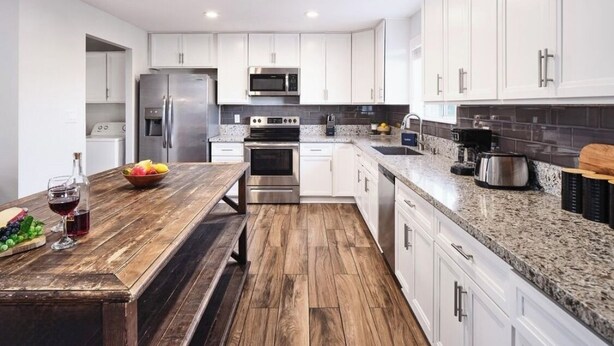A modern kitchen with white cabinets, stainless steel appliances, and a wooden dining table. - Old Town Scottsdale Retreat: 5BD, 2BA with a Pool, BBQ Grill, & More (Scottsdale)