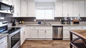 A modern kitchen with white cabinets, stainless steel appliances, a granite countertop, and a wooden floor. - Old Town Scottsdale Retreat: 5BD, 2BA with a Pool, BBQ Grill, & More (Scottsdale)