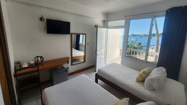 Ein Hotelzimmer mit Bett, Schreibtisch mit Wasserkocher, Fernseher und einem Balkon mit Meerblick.