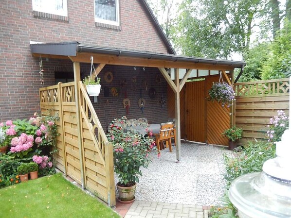 A covered patio area with a wooden gate, a seating arrangement, and a brick wall with decorative elements.