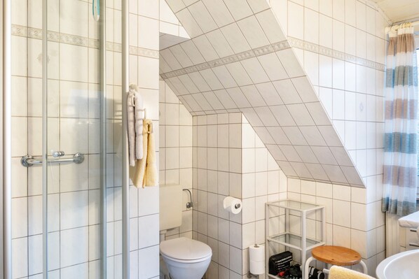 Une salle de bain avec une douche à parois de verre, des toilettes, un lavabo et un tabouret en bois.