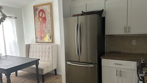 A modern kitchen with a stainless steel refrigerator, white cabinets, and a dining area with a table and cushioned chair. - Beautiful  2-bedroom/2-bath condo with AC close to beach & shopping in  Naples (Naples)