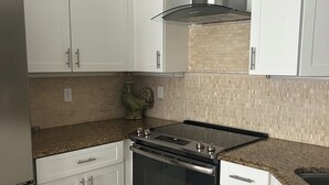 A kitchen with white cabinets, a stainless steel stove, and a granite countertop. - Beautiful  2-bedroom/2-bath condo with AC close to beach & shopping in  Naples (Naples)